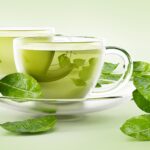 Glass cups with green tea and tea leaves isolated on white