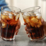 Women,Holding,Glasses,Of,Cola,With,Ice,At,Table,,Closeup