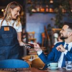 Smiling,Man,In,A,Suit,Engages,With,A,Waitress,,Using